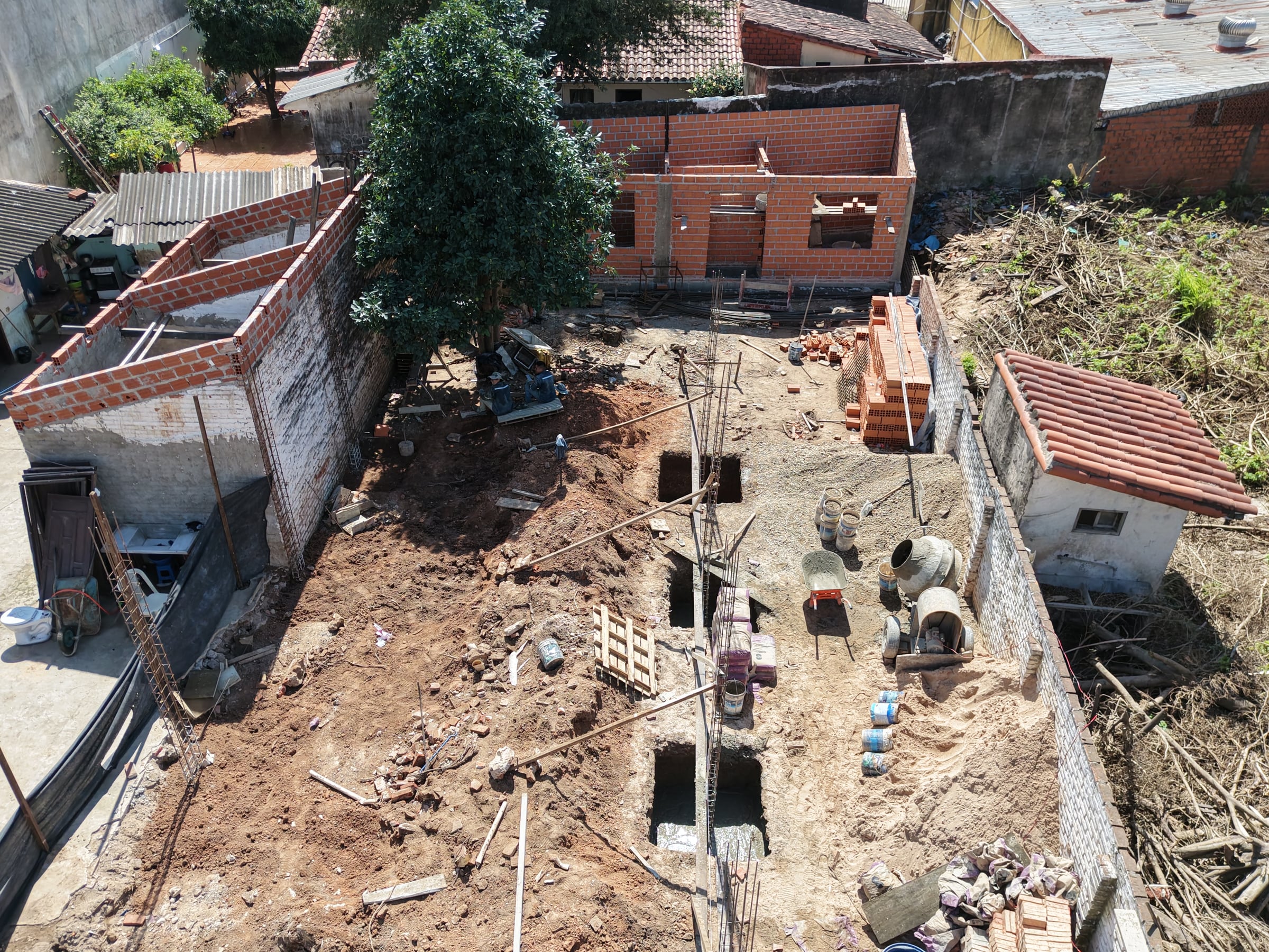 Vista aérea de la obra: zapatas excavadas y hormigonadas, columnas de hierro armadas y el muro perimetral de ladrillo levantado.
