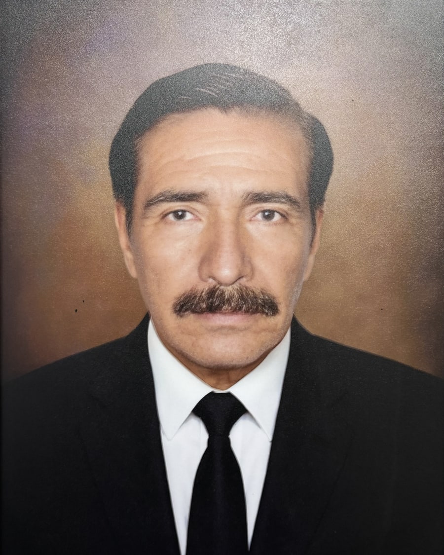 Retrato de estudio del profesor Reinaldo Suca Zambrana, de traje oscuro y corbata, mirando a cámara.