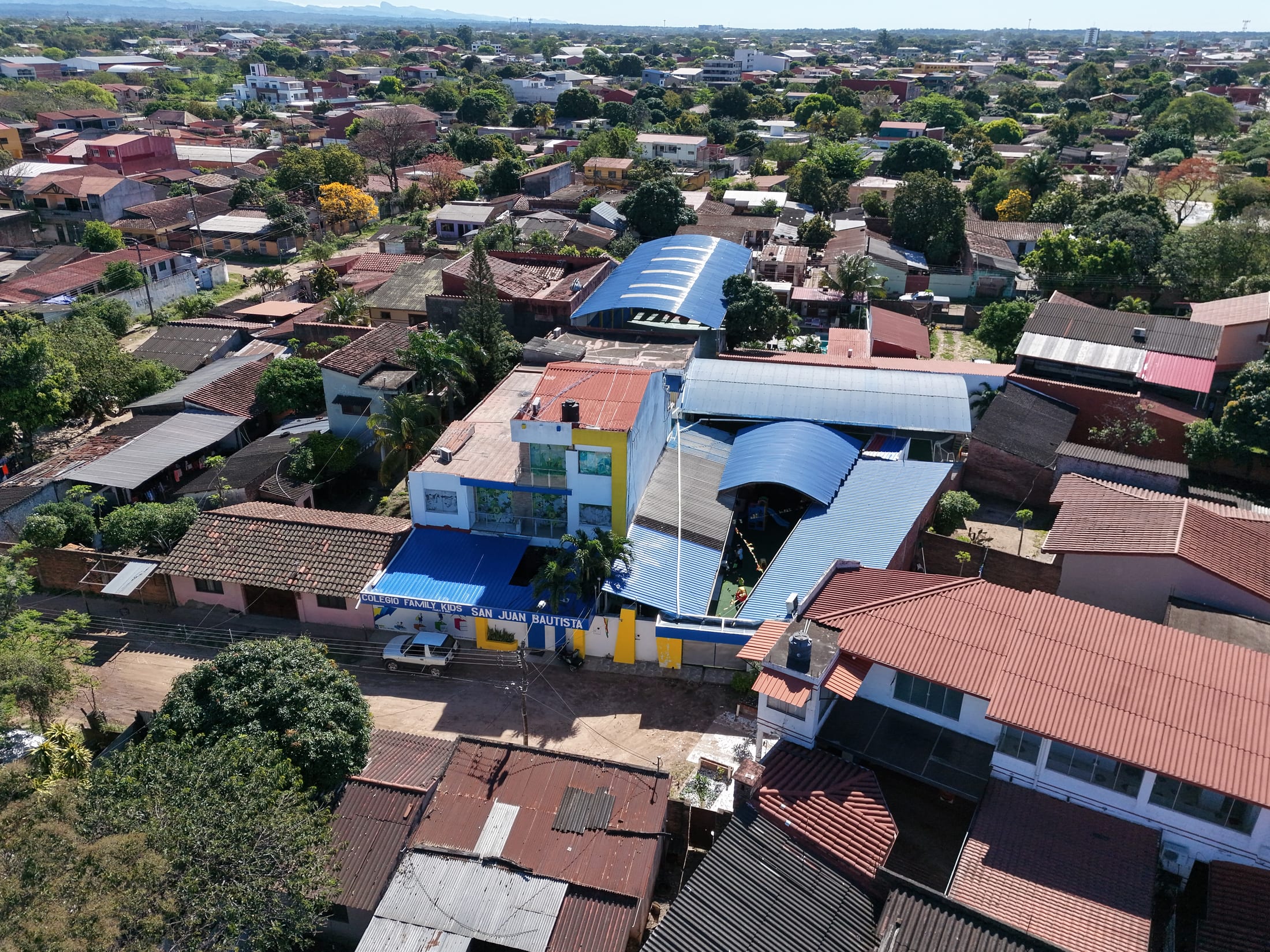 Vista aérea amplia del barrio de San Juan Bautista con el colegio y la ciudad en el horizonte.