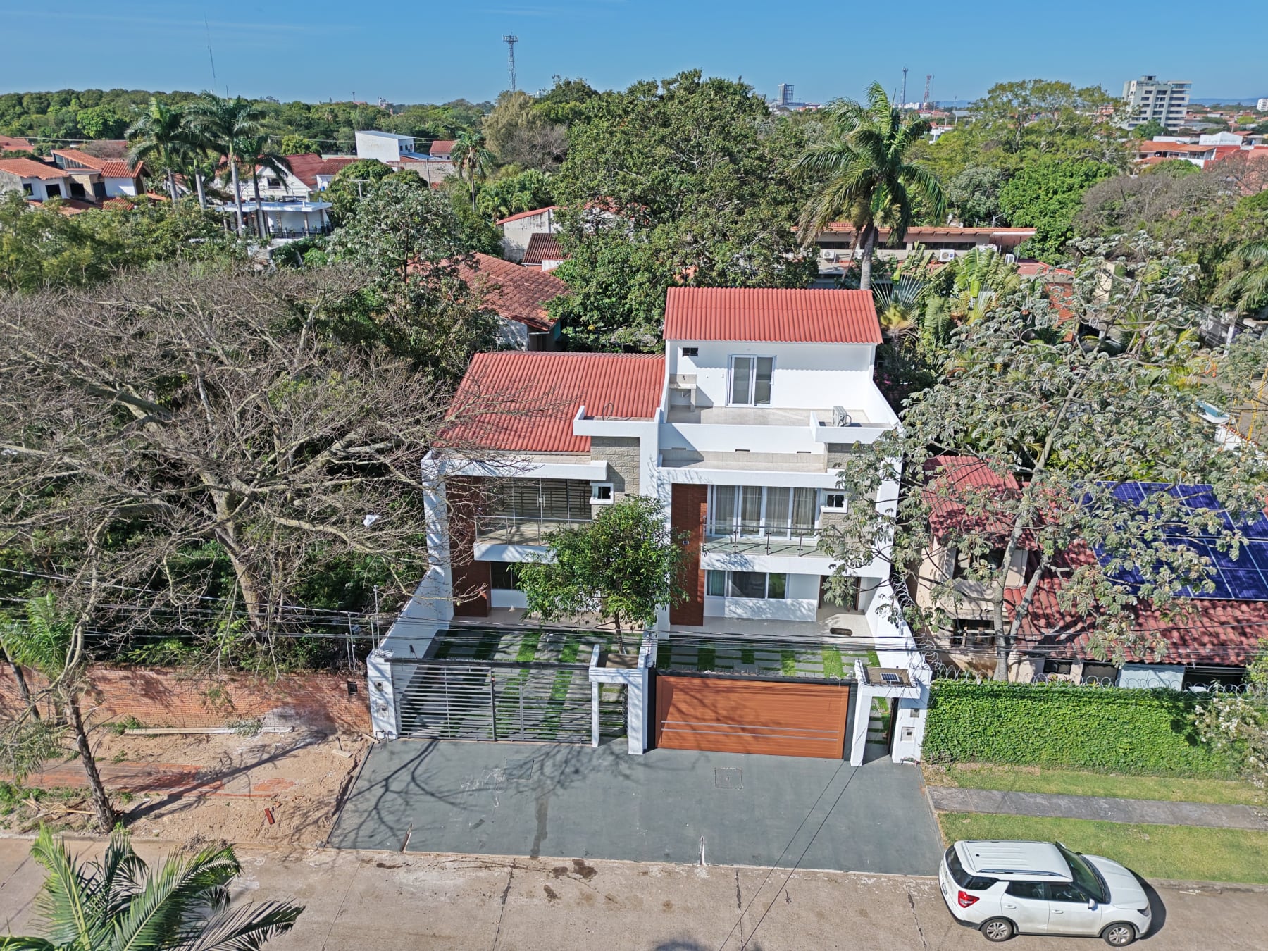 Vista aérea de la casa que Grupo Suca entregó en Av. Roca y Coronado: tres niveles, estucado blanco, revestimiento de piedra y carpintería de madera, con el arbolado del barrio y la ciudad al fondo.