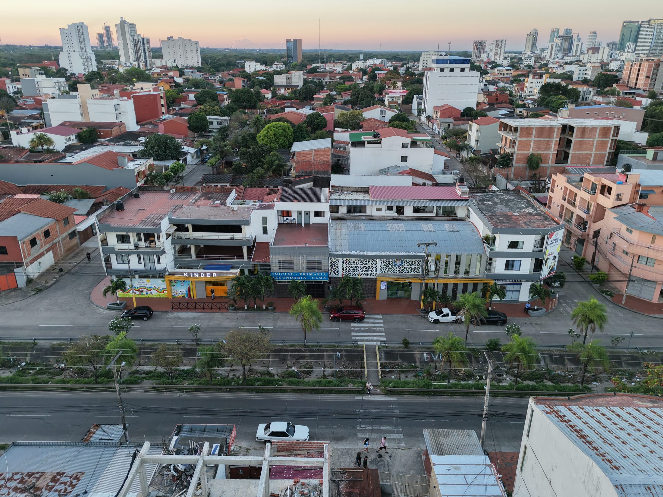Vista aérea del Colegio Savia Nueva al atardecer, sobre la avenida, con la ciudad al fondo.
